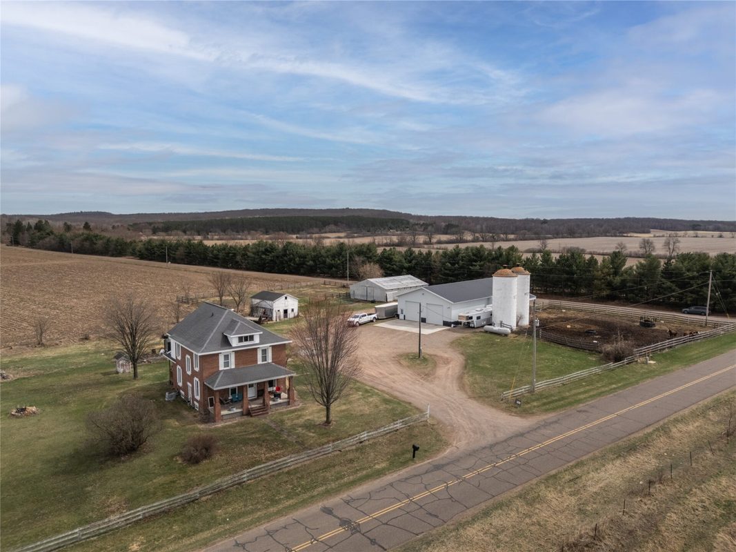2003 23rd Street, Rice Lake WI 54868 - Aerial of brick farmhouse, white metal shop, two silos, and fenced horse paddock along rural road - MLS #1598985 - image2