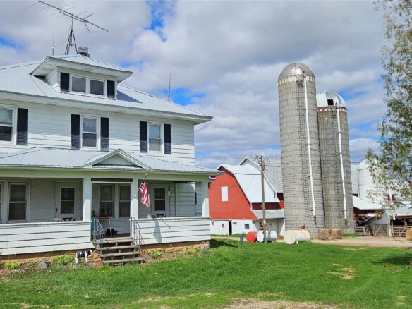 E12088 Cty. Rd. K, Augusta WI 54722 - Two-story white farmhouse with covered front porch, black shutters, two concrete silos and red barn behind - MLS #1600657 - image1
